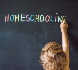 Homeschooling. Child pointing at word Homeschooling on a blackboard.