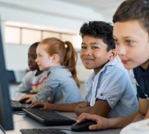 Multiethnic school kids using computer in classroom at elementary school. Portrait of arab boy looking at camera in a computer room. Smiling primary student in a row using desktop pc in class room.