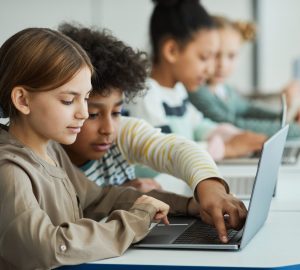 Side view at diverse group of children sitting in row at school classroom and using laptops